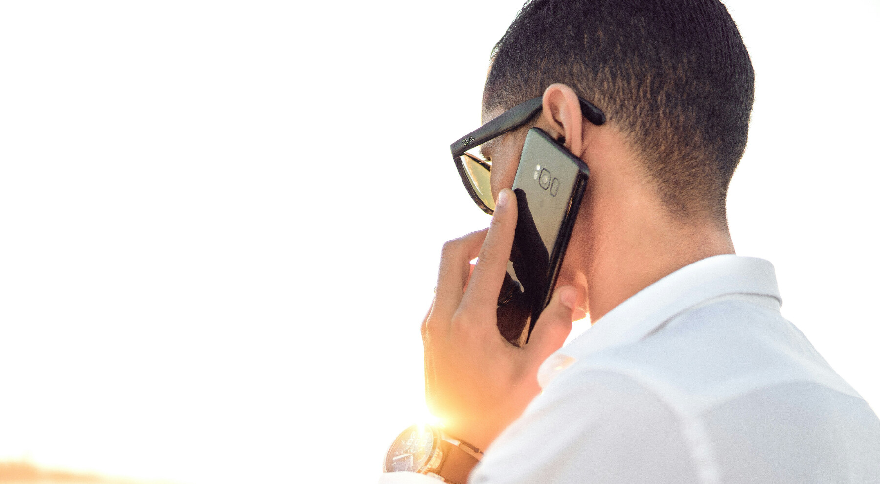 Egy úriember a telefonját a füléhez rakva kommunikál a napsütéses időben.